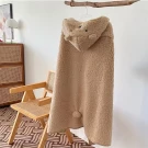 A beige teddy hoodie blanket with bear ears and a pom-pom hangs on a rod above a wooden chair.