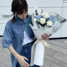 Woman in denim holding a white and blue bouquet of roses, hydrangeas, and eucalyptus.