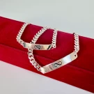Two silver chain bracelets with infinity symbols on rectangular charms, resting on a red velvet box.