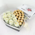 Heart-shaped box with white roses and Ferrero Rocher chocolates, tied with a ribbon.
