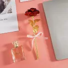 Gold-stemmed red rose with a pink ribbon, next to a perfume bottle and laptop.