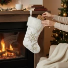 White Christmas stocking with gold snowflakes being filled with a gift.