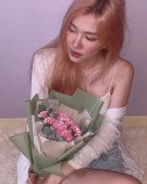 Woman holding a bouquet of pink carnations and dusty miller, wrapped in green paper.