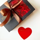 Chocolate-covered strawberries and red artificial roses arranged in a black gift box.