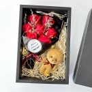 A gift box with red soap roses, a teddy bear keychain, and fairy lights.