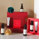 Red gift box with skincare bottles, a tube, and a blue decorative flower.