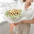 Bouquet of 19 Ferrero Rocher chocolates surrounded by white gypsophila, tied with a peach ribbon.