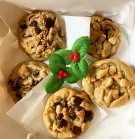 Five Christmas chocolate chip cookies arranged in a box with decorative holly and berries.