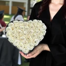 Heart-shaped box of cream roses with diamond centers, held by a person in a graduation robe.
