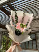 Pink roses and eucalyptus bouquet wrapped in white and pink paper, tied with a pink ribbon.