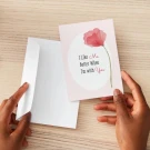 Hands hold a pink card with a red poppy and "I Like Me Better When I'm With You" text next to a white envelope.