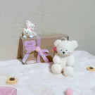 Three white teddy bear figures on a gift box and a large white teddy bear candle.