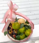 Pink basket filled with pears, mangosteens, oranges, and green leaves, tied with a pink bow.