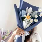 Crocheted daffodil, blue, and white tulip bouquet in navy wrapping.