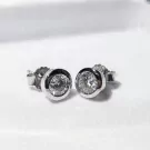 Pair of white gold stud earrings with round-cut moissanite diamonds in a bezel setting.