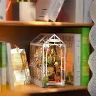 A miniature greenhouse book nook with plants, chair, and lamp, on a shelf with books.