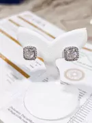 Cushion-cut moissanite diamond earrings in a halo setting, displayed on a white stand.