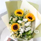 Three sunflowers with white statice flowers in a light green and cream bouquet wrap.