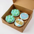 Box of four Mother's Day cupcakes: two with blue floral frosting, one with a blue heart saying "love", and one decorated with "MOM".