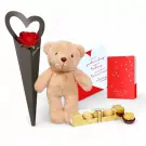 A teddy bear, red rose, Ferrero Rocher chocolates, and two love cards on a white background.