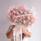 A bouquet of rose-shaped banknotes and baby's breath, wrapped in pink paper.