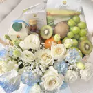 A fruit and flower basket with Doi Kham products and white roses.