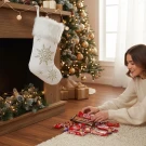 Woman fills a white snowflake Christmas stocking with candy, with a decorated tree in the background.