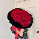 99 red roses arranged in a heart shape, a large bouquet with black wrapping and a red bow.