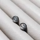 Pair of 0.5-carat round-cut moissanite diamond stud earrings set in silver on a textured white surface.
