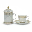 Pearlized ceramic mug with lid and gold trim, next to a matching coffee cup and saucer.