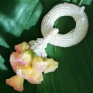 A white flower garland with yellow and pink flowers on green leaves.