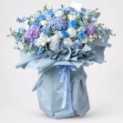 Luxury Ocean Dreams Bouquet: blue hydrangeas, roses, and white flowers wrapped in blue paper, tied with a blue ribbon.