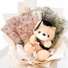 A graduation teddy bear with a cap and gown in a bouquet with Thai baht banknotes.
