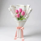 Pink velvet tulips in a white bouquet wrap, tied with a pink ribbon.