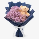 Teddy bear peeking through pink limonium flowers in a navy and black bouquet tied with a white ribbon.