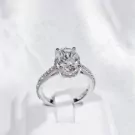 Silver oval-cut moissanite ring with paved band on a white stand.