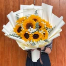 A bouquet of ten bright sunflowers, white baby's breath, and eucalyptus leaves in cream wrapping.