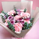 Pink carnations and purple mums arranged in a bouquet with eucalyptus, wrapped in paper.