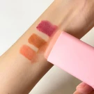 Swatches of three lipsticks in pink, brown, and berry shades on an arm.