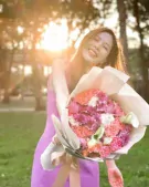 Woman in purple dress smiles holding a bouquet of pink, orange, and white flowers.