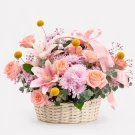 A woven basket overflowing with pink lilies, peach roses, and purple mums, adorned with a pink ribbon and small yellow accents.
