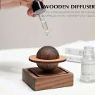 Wooden planet diffuser with dropper adding oil, beside a small bottle.