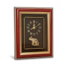 Framed clock with Roman numerals and gold elephant figurine on dark brown background.