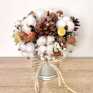 Cotton flower and pine cone arrangement in a metal bucket, tied with twine.