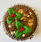 Decadent 6-inch Valrhona chocolate brownie topped with chocolate chips, white chocolate chunks, almonds, and festive holly sprigs in a foil pan.