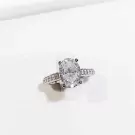 Oval-cut moissanite diamond ring with pavé band on white background.