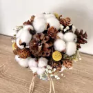 Round bouquet of cotton flowers, pine cones, and small yellow flowers in a metal pot.