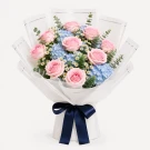 Pink roses and blue hydrangeas bouquet with white wrapping and ribbon.