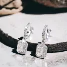 Silver drop earrings with two large emerald-cut moissanite diamonds surrounded by smaller stones.