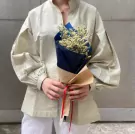 Person holding a mini-bouquet of yellow limonium flowers wrapped in craft and navy paper.